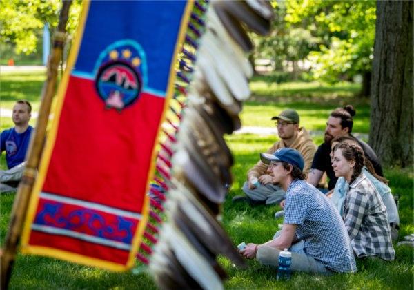 students seated in a circle, Native banner with feathers at right