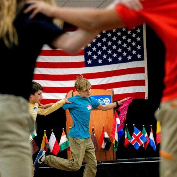 sixth graders dancing in a circle, American flag in background, small country flags on display also